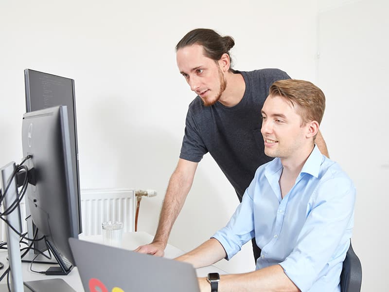 Luis und Max vor mehreren Bildschirmen, in die Arbeit vertieft.